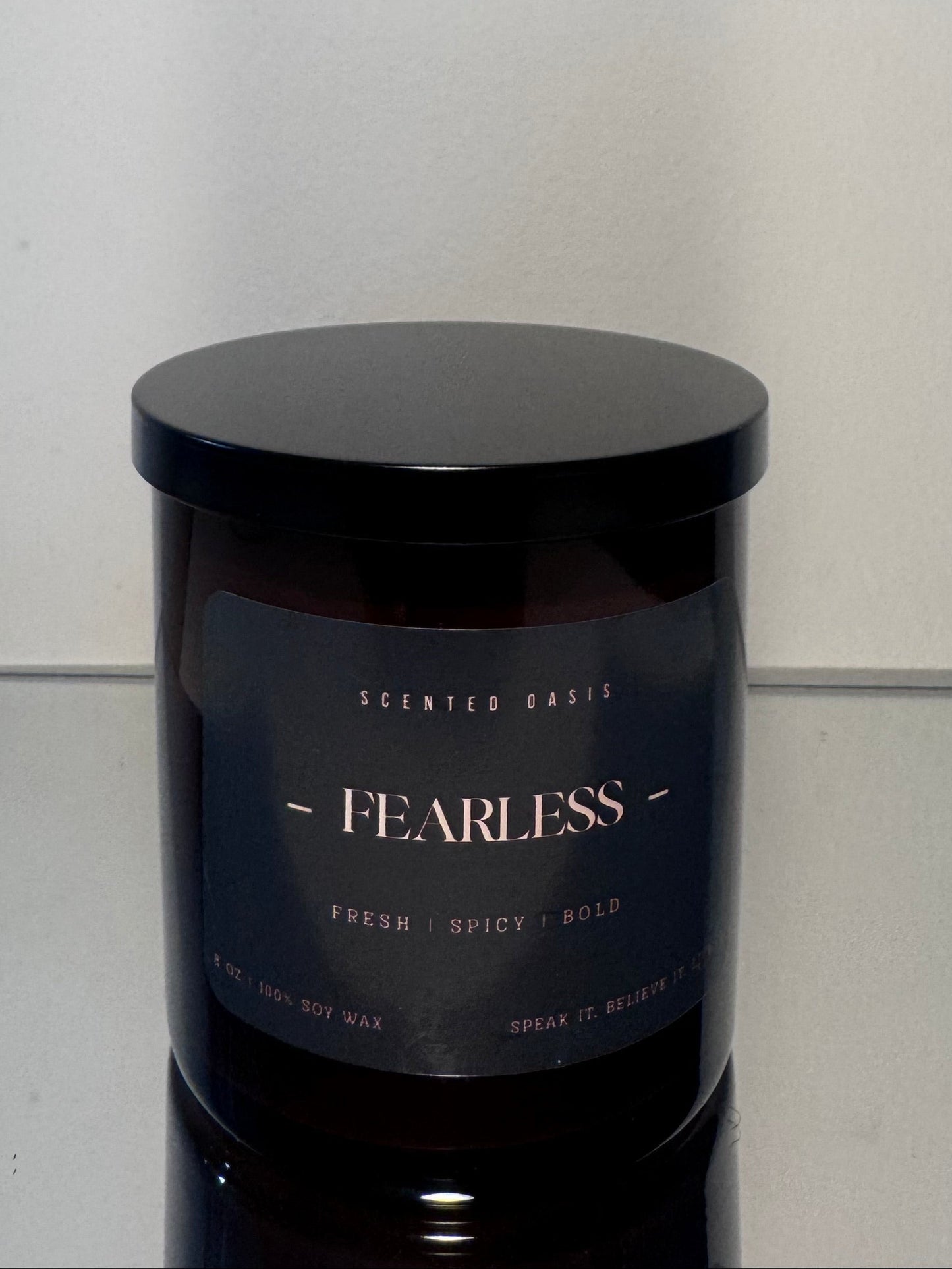 A dark amber glass jar candle with a black lid and a black label reading 'SCENTED BAKS - FEARLESS -' on a light gray surface against a light gray background.