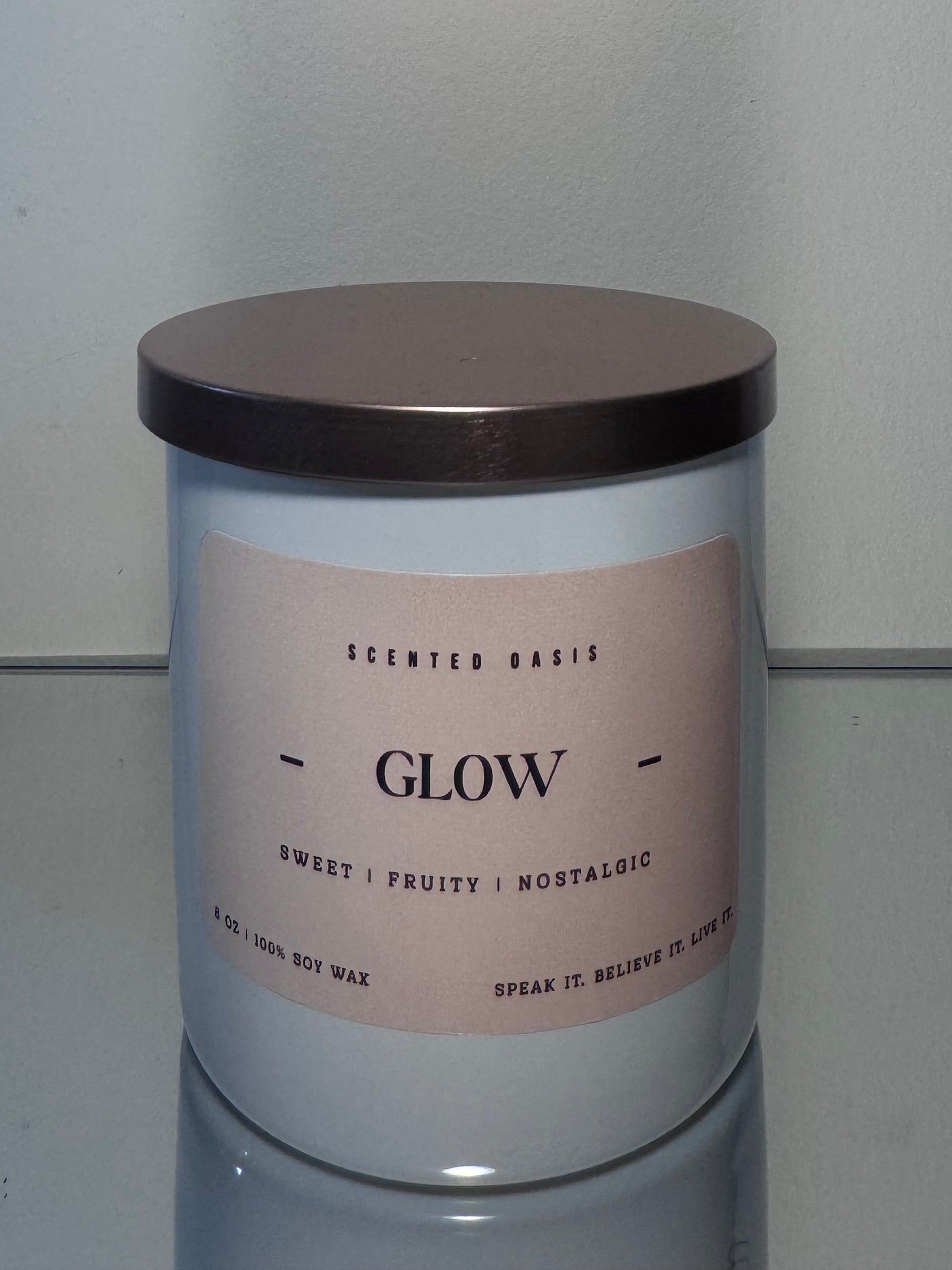A white glass jar candle with a metallic bronze lid and a pale pink label reading 'SECRETS BAKE' and 'GLOW'.
