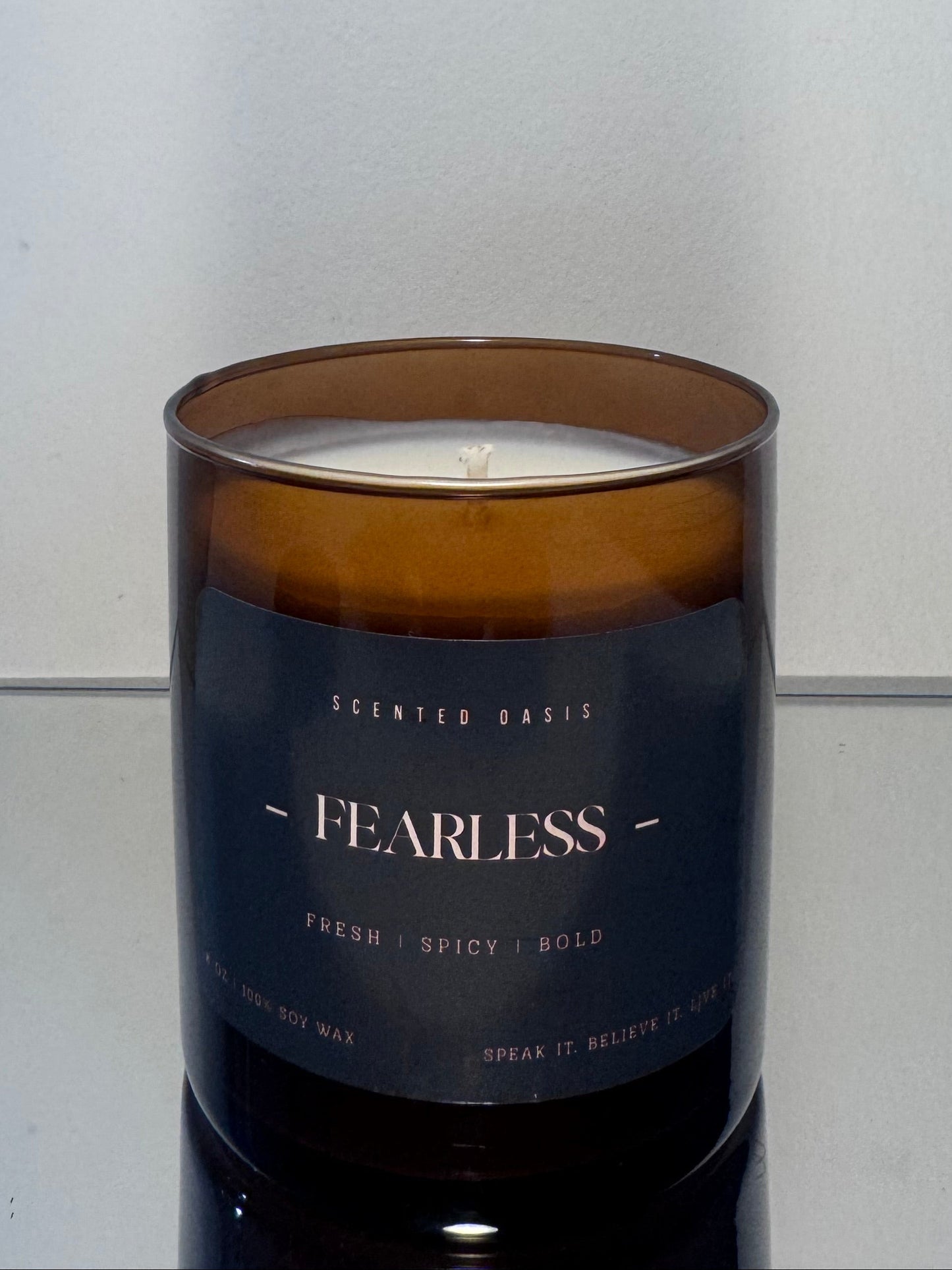 A scented candle in an amber glass jar with a dark navy label reading 'FEARLESS' and 'SCENTED BARKS', photographed against a plain light gray background.