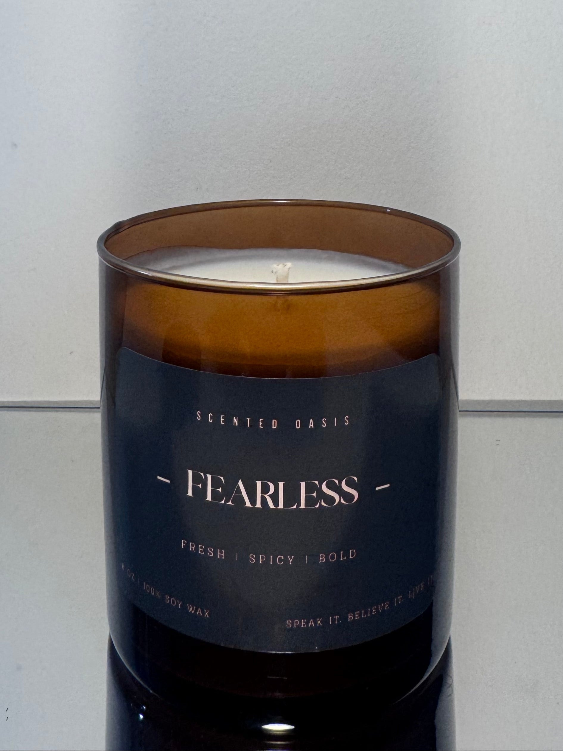 A scented candle in an amber glass jar with a dark navy label reading 'FEARLESS' and 'SCENTED BARKS', photographed against a plain light gray background.